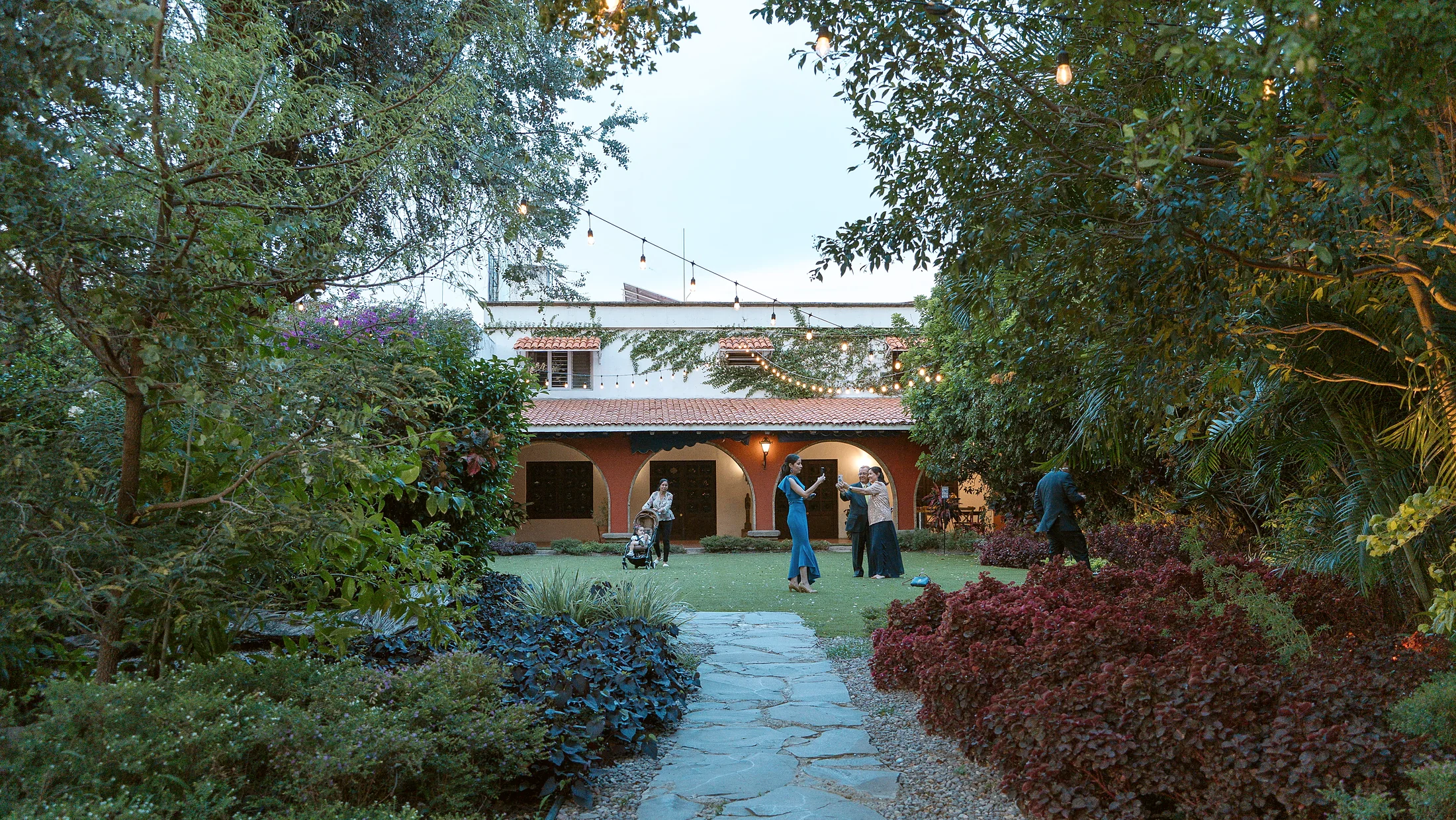 El jardín al atardecer: camino de piedra entre arriates, con la casona y sus arcos al fondo